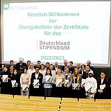 Personen stehen auf der Bühne vor der Projektionsfläche 