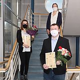 Menschen mit Blumen halten eine Urkunde und stehen auf einer Treppe 