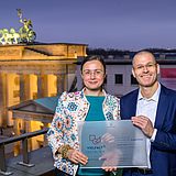 Zwei Personen vor dem Brandenburger Tor mit einem Vielfalt-Zertifikat